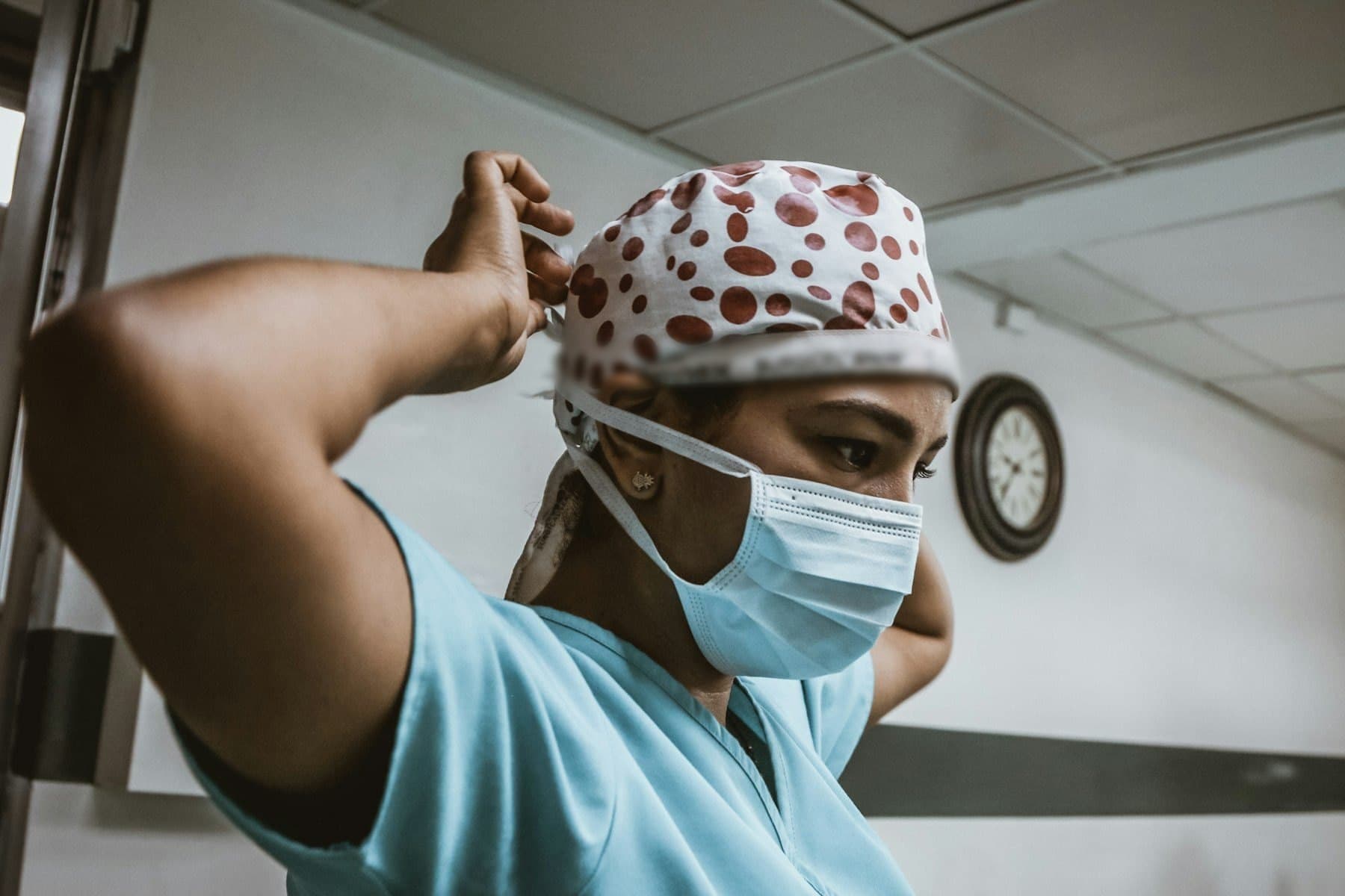A clinician tying her surgical cap before a list, mask already on.