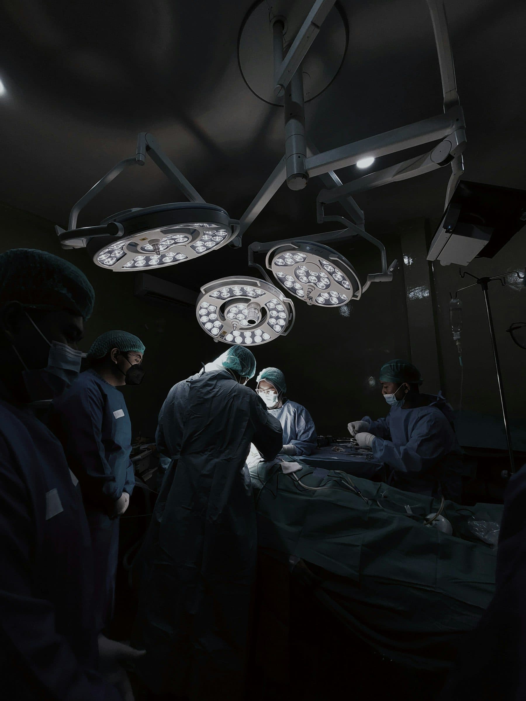 An operating theatre lit only by its overhead lamps, the team in silhouette.